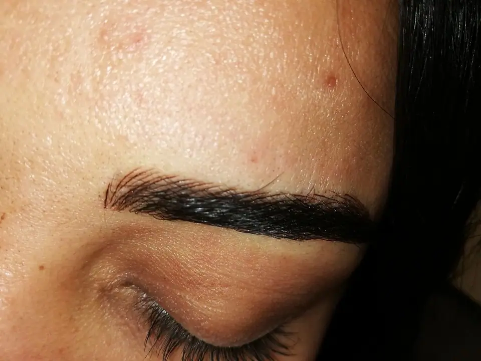 Primer plano de una ceja con micropigmentación tipo microblading, con trazos finos imitando pelo