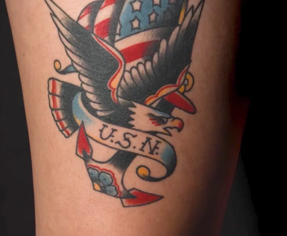 Tatuaje tradicional a color de un águila con ancla y la leyenda U.S.N., estilo marinero