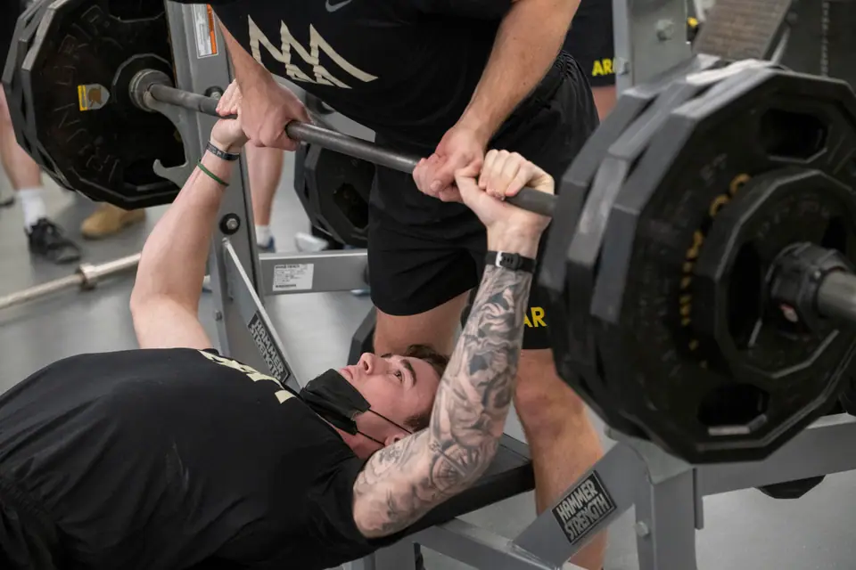 Hombre con tatuajes en los brazos haciendo press de banca con barra en un gimnasio