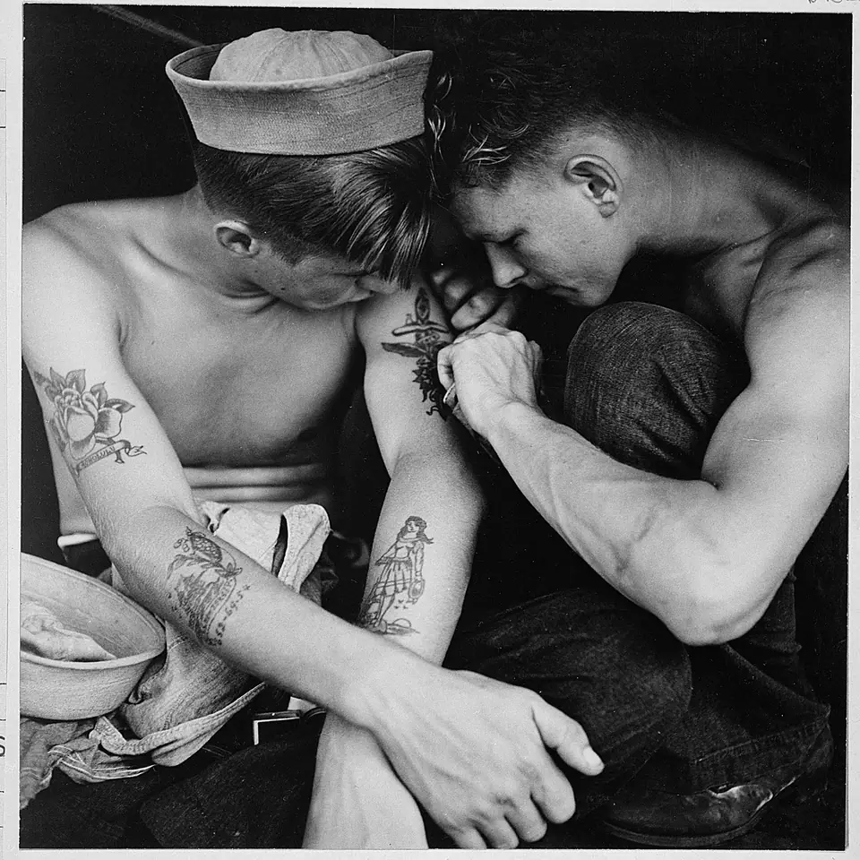 Foto histórica de un marinero muy tatuado a bordo del USS New Jersey, mientras le tatúan el brazo
