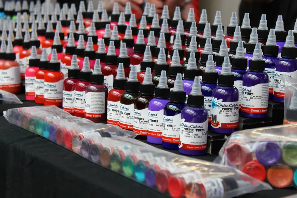 Hileras de botellas de tinta de tatuaje de distintos colores en un puesto de convención