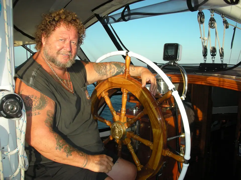 Marinero con tatuajes en el brazo al timón de un barco