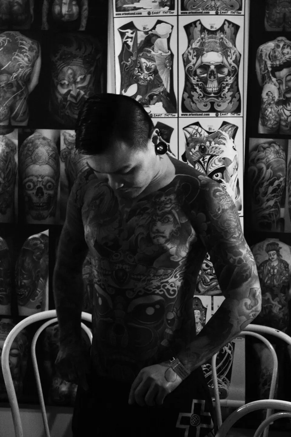 Hombre con tatuajes de cuerpo completo frente a una pared con diseños flash